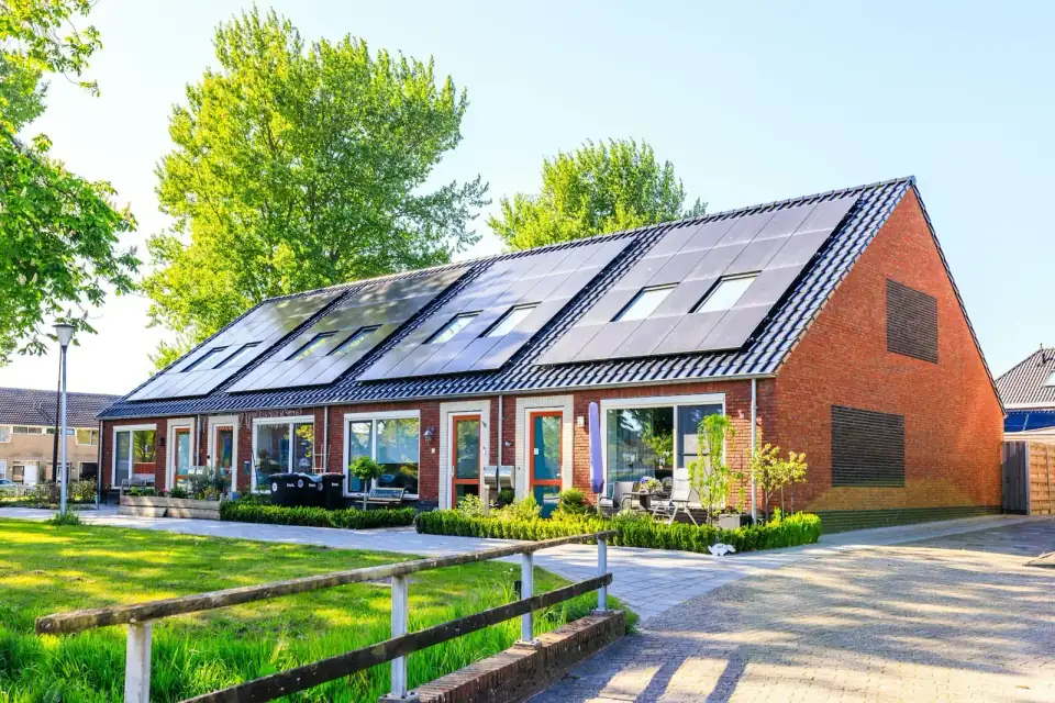 Een rij nieuwe rijtjeshuizen van rode baksteen met zwarte zonnepanelen op de daken, op een zonnige dag